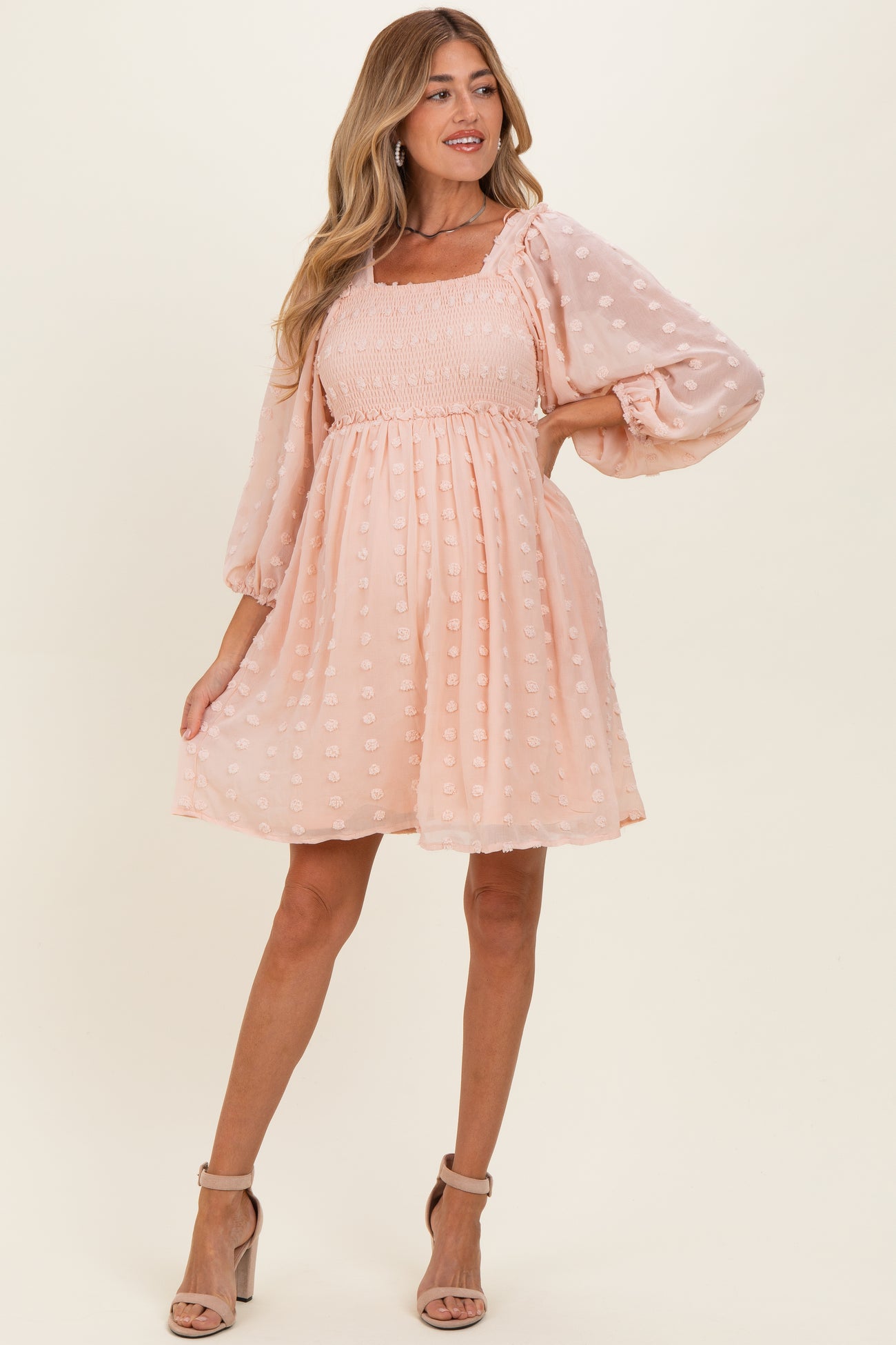 woman wearing a light pink maternity dress with puff sleeves and textured polka dots, styled in a flared design
