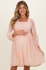 woman wearing a soft pink maternity dress with dot details and puff sleeves, holding her baby bump