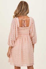 woman wearing a blush pink maternity dress with puff sleeves and smocked back detail