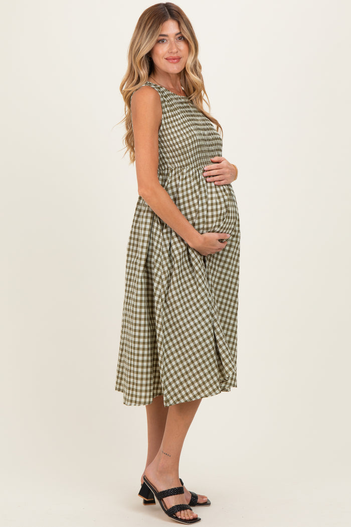 woman wearing a green and white gingham maternity dress and holding her baby bump