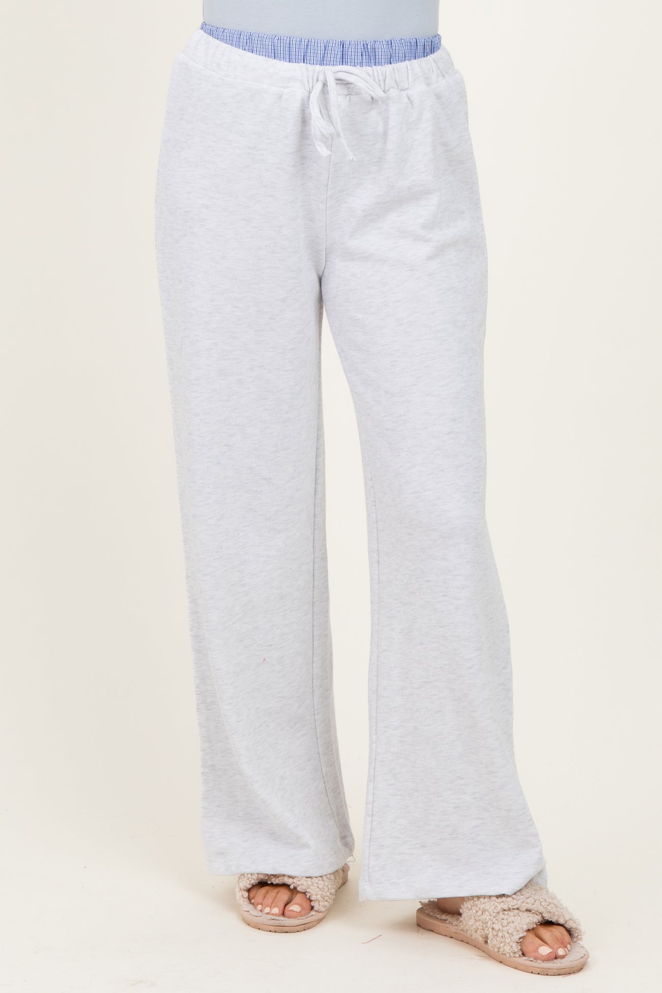 woman wearing light gray lounge pants with a drawstring waistband and a relaxed fit, paired with fuzzy slippers