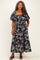 plus size woman wearing a black floral maxi dress with a square neckline and puff sleeves, standing with hands in pockets