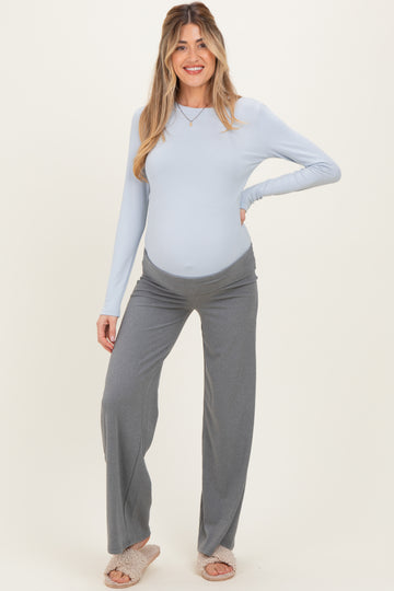 woman wearing a light blue long sleeve maternity top and gray wide-leg pants, showing off her baby bump