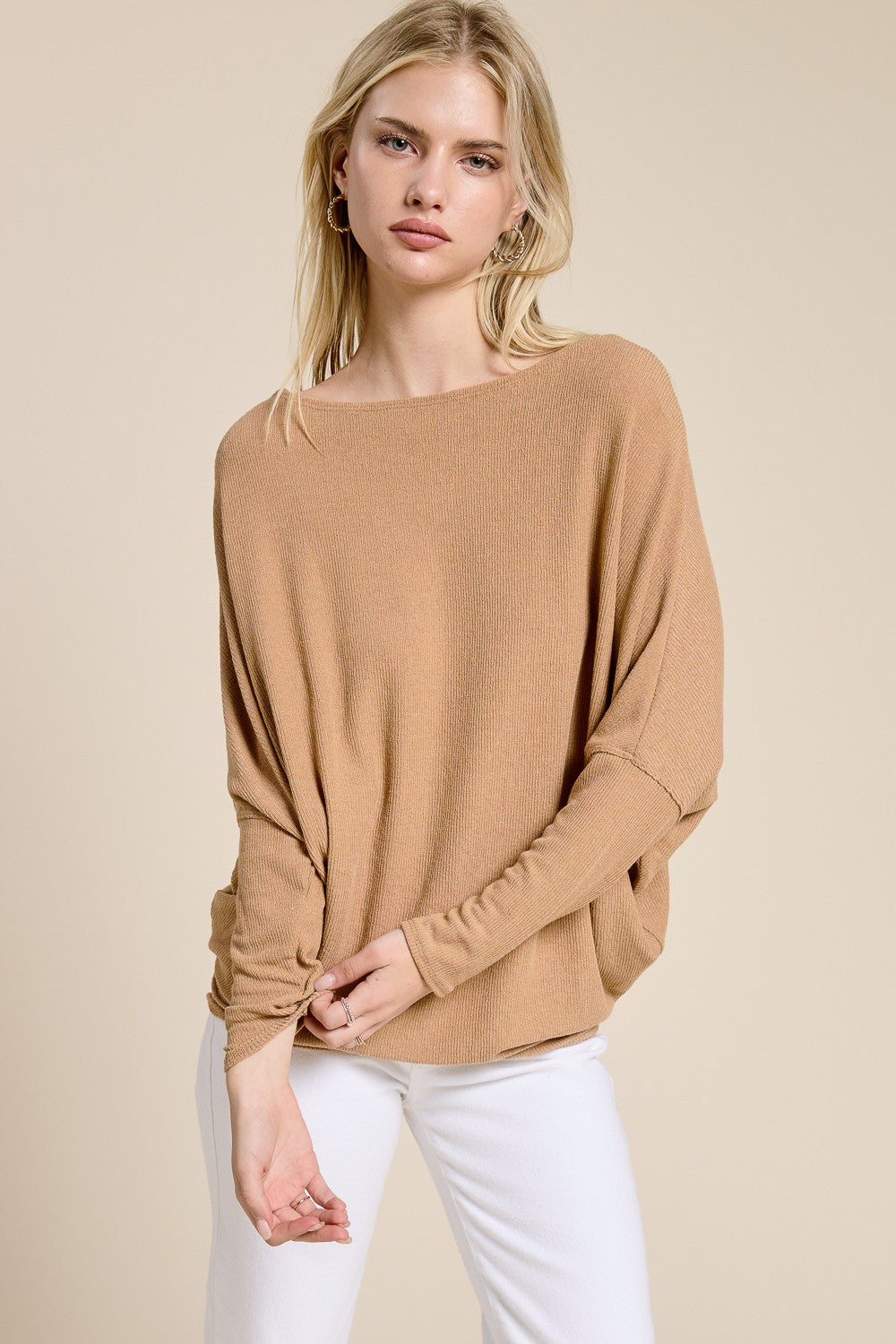 woman wearing a camel long sleeve oversized top with a boat neckline and relaxed fit paired with white pants