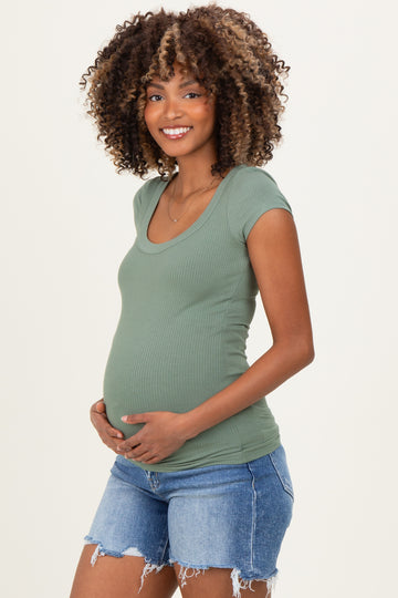 woman wearing a green short sleeve maternity top and holding her baby bump, paired with denim shorts