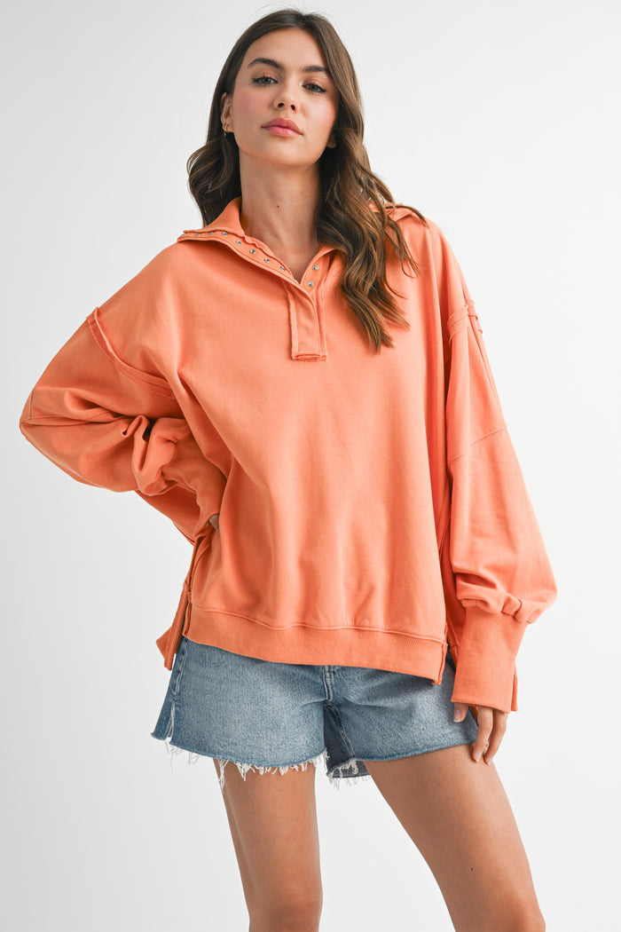 woman wearing an oversized coral pullover sweatshirt with a half-zip collar and paired with denim shorts