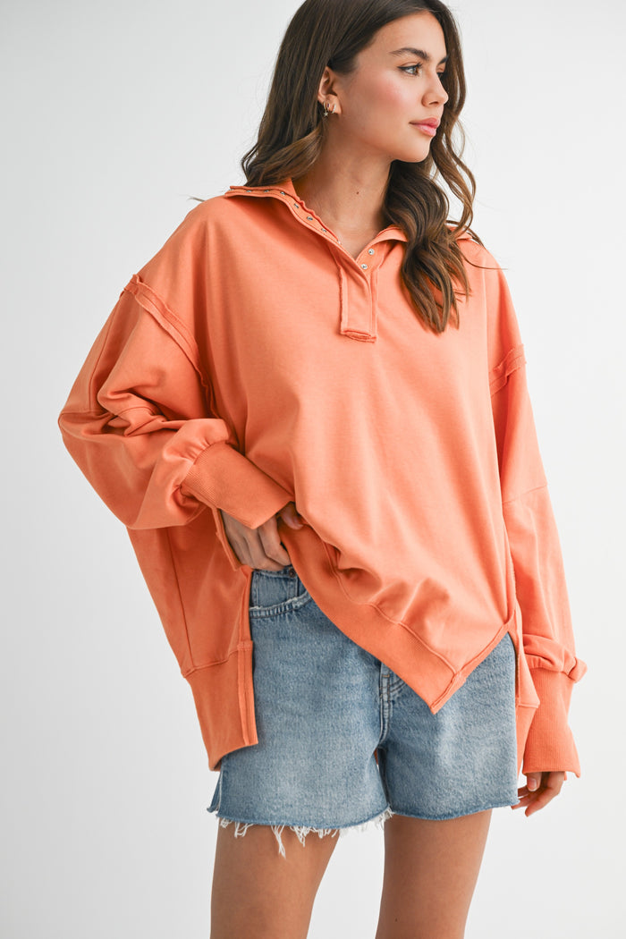 woman wearing an oversized orange pullover shirt with a collar and distressed denim shorts
