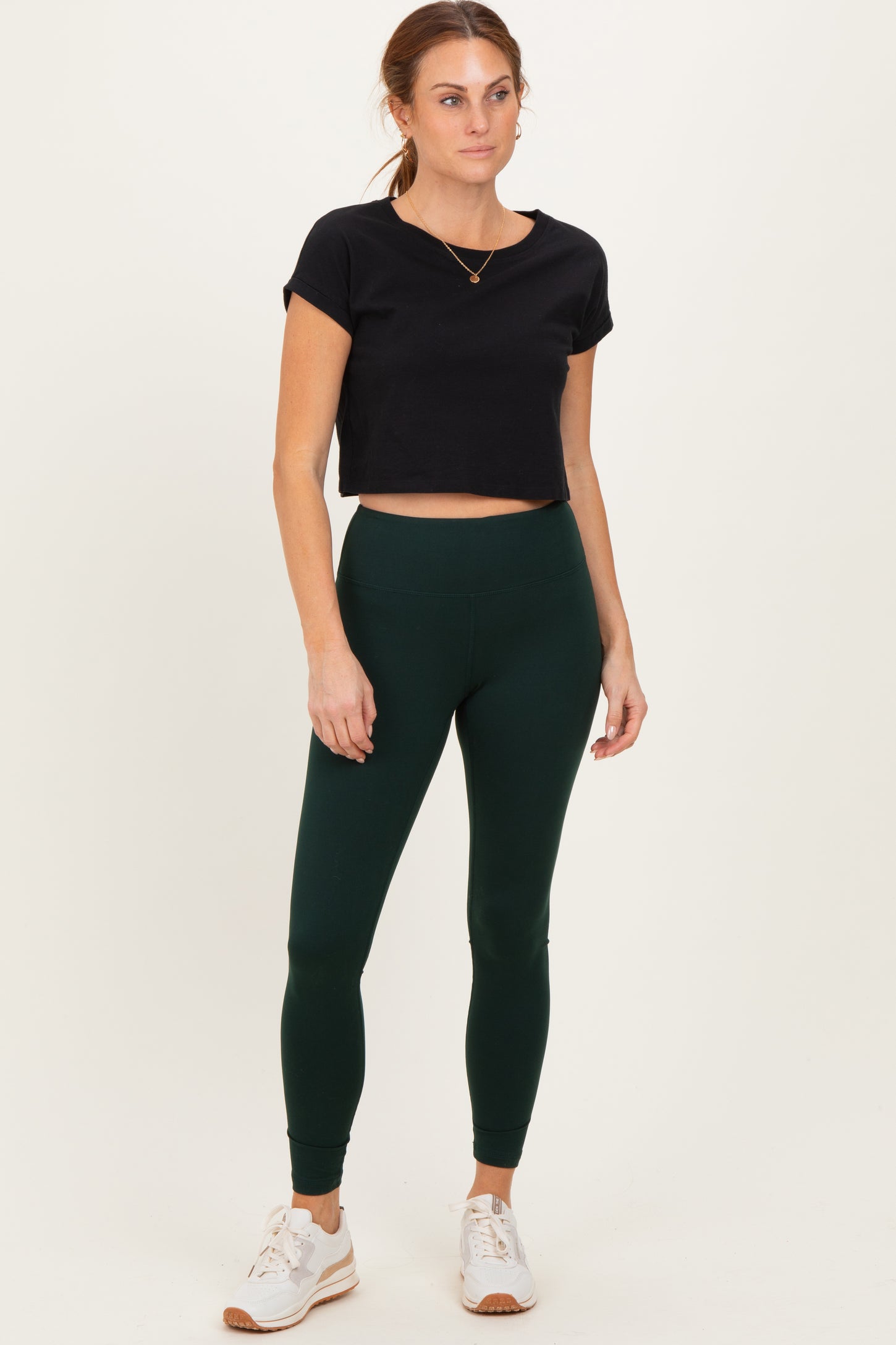 woman wearing a black cropped t-shirt and dark green leggings, paired with white athletic shoes