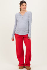 woman wearing a gray maternity long sleeve henley top and red maternity wide leg pants with a visible baby bump
