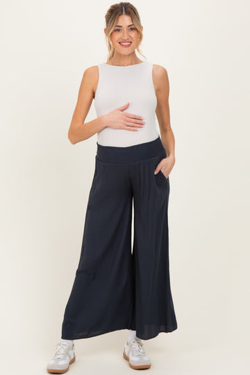 woman wearing a white maternity tank top and navy wide-leg maternity pants, holding her baby bump