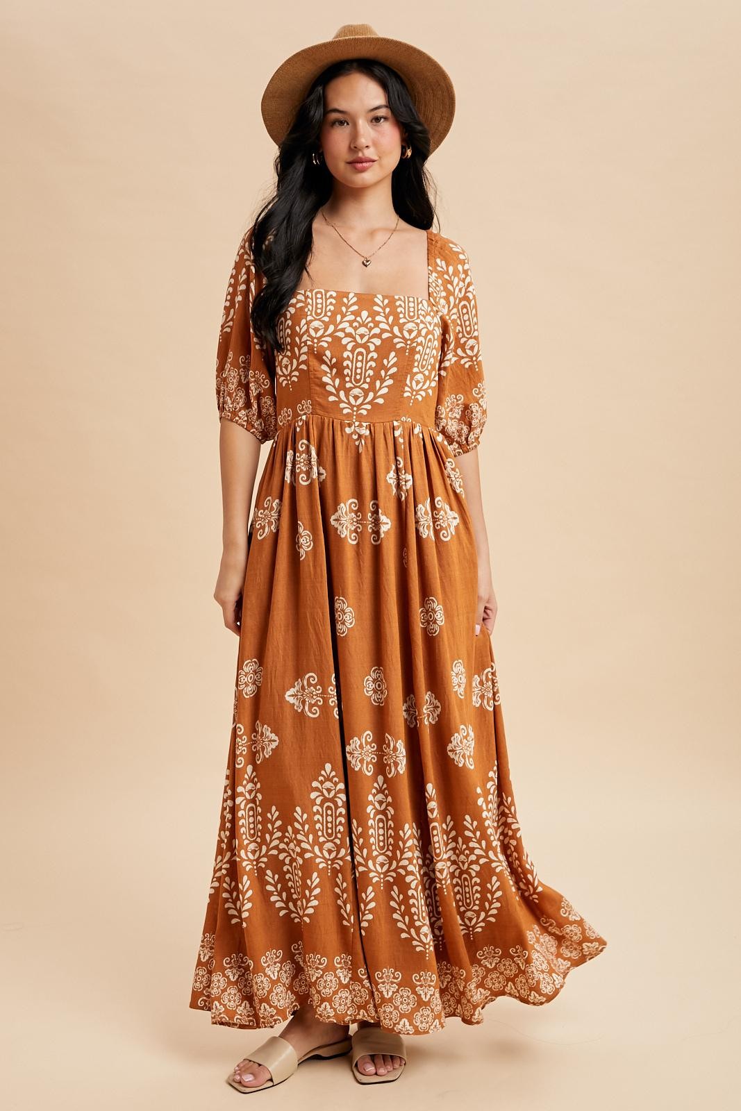 woman wearing a rust brown floral maxi dress with puff sleeves and a square neckline, styled with a hat