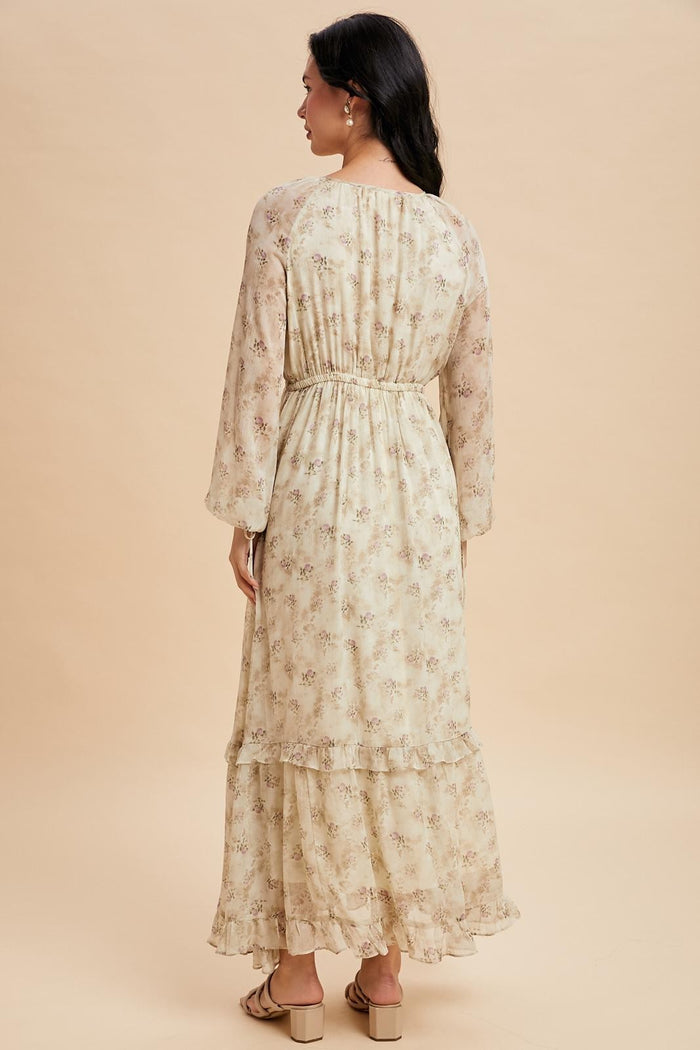 woman wearing a long sleeve beige floral maxi dress with a tiered skirt and an elastic waist, viewed from the back