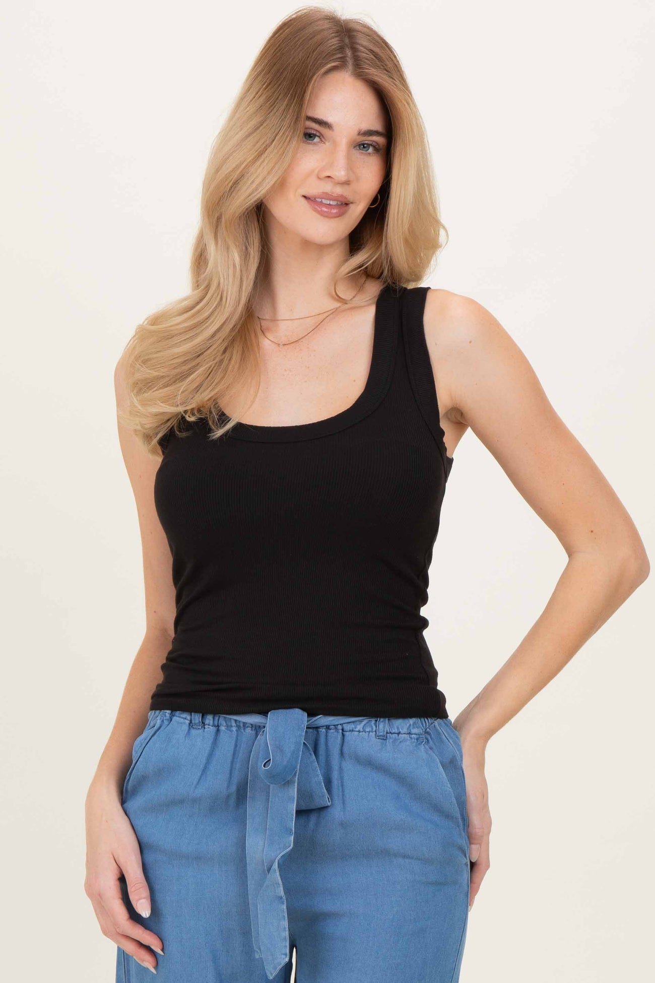 woman wearing a black ribbed tank top with a scoop neckline and styled with light blue high-waisted pants