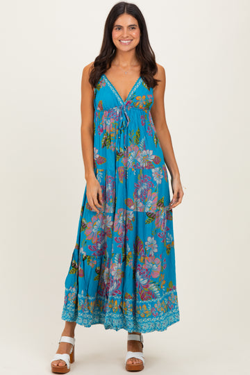 woman wearing a turquoise floral maxi dress with a v-neck and tie detail, standing and smiling