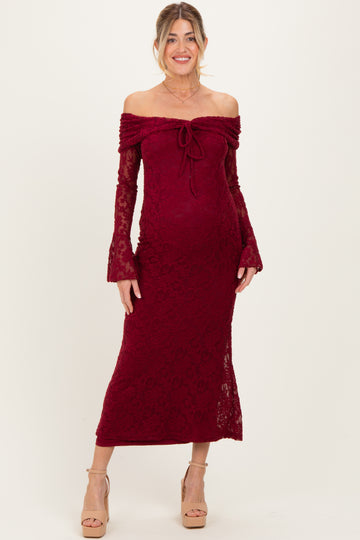 woman wearing a burgundy off-the-shoulder lace maternity dress with bell sleeves and a tie detail, showing her baby bump