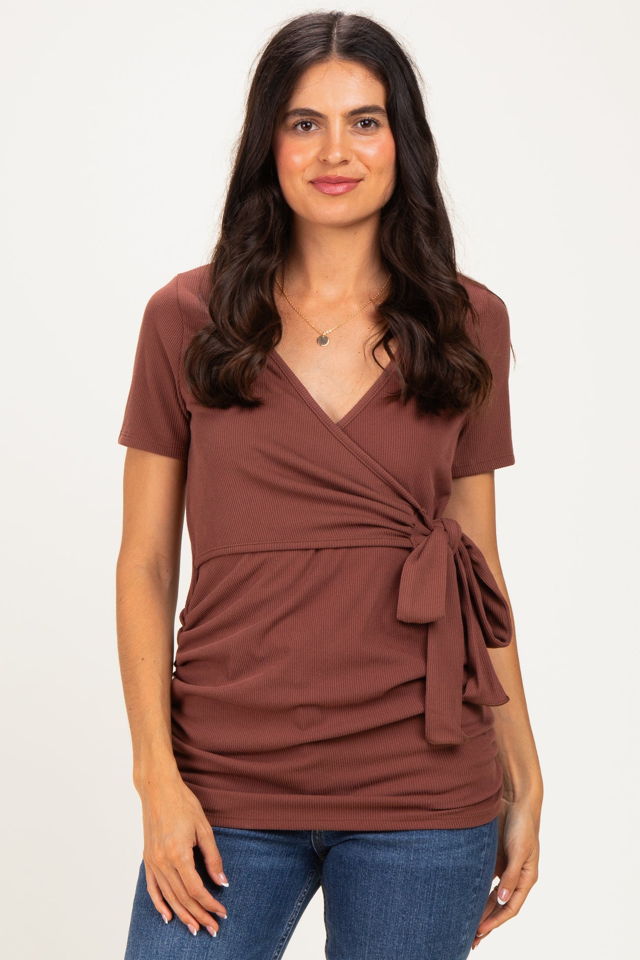 woman wearing a rust-colored short sleeve wrap top with a tie detail at the waist and jeans