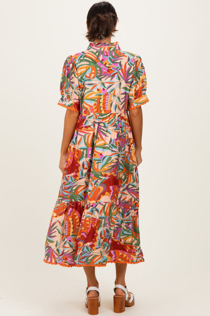 woman wearing a colorful floral print midi dress with puff sleeves and a ruffled hem, standing with her back to the camera