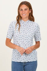 woman wearing a light blue short sleeve floral top with a ruffled neckline and smiling