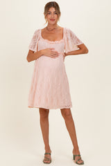 woman wearing a pink lace maternity dress with short puff sleeves and a visible baby bump