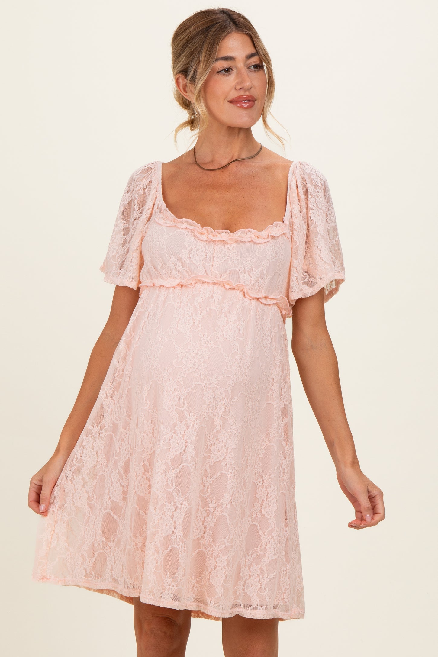 woman wearing a light pink lace maternity dress with short puff sleeves and ruffled detailing, showcasing a baby bump