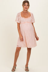 woman wearing a light pink lace maternity dress with short sleeves and a ruffled neckline, showing a baby bump