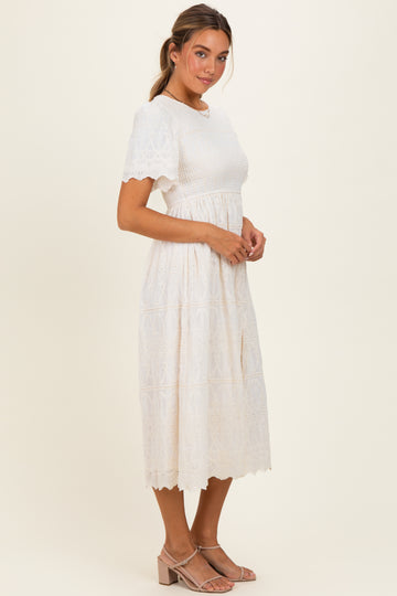 woman wearing a white embroidered midi dress with short sleeves and a cinched waist, paired with strappy sandals