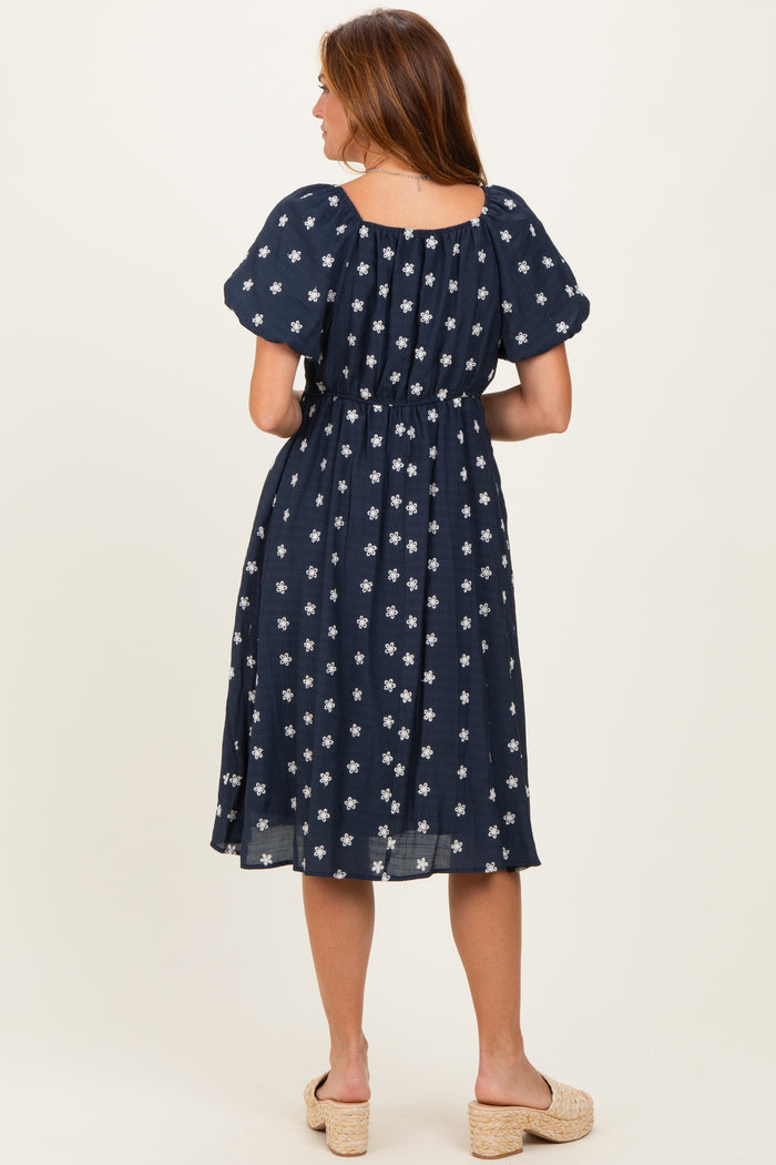 woman wearing a navy blue midi dress with white floral patterns and puff sleeves, seen from the back