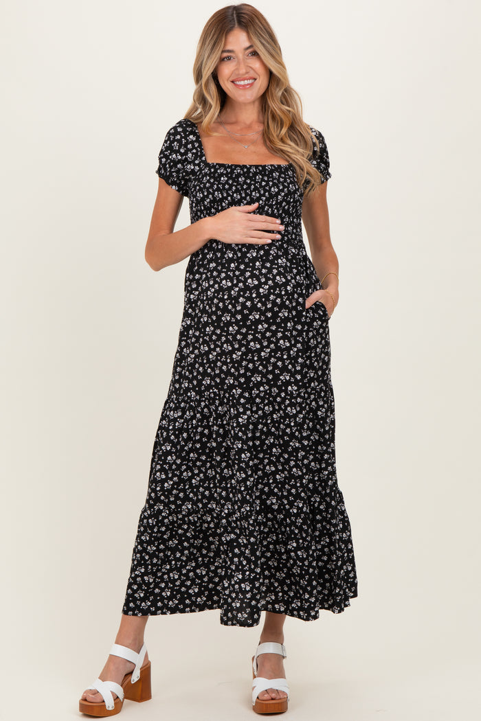 woman wearing a black floral maternity maxi dress, holding her baby bump and smiling
