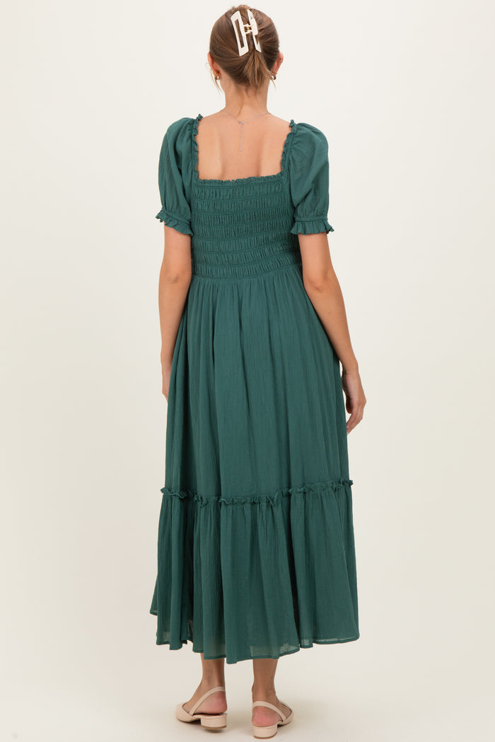 woman wearing a green maternity dress with puffed sleeves and a tiered hem, showing the back view
