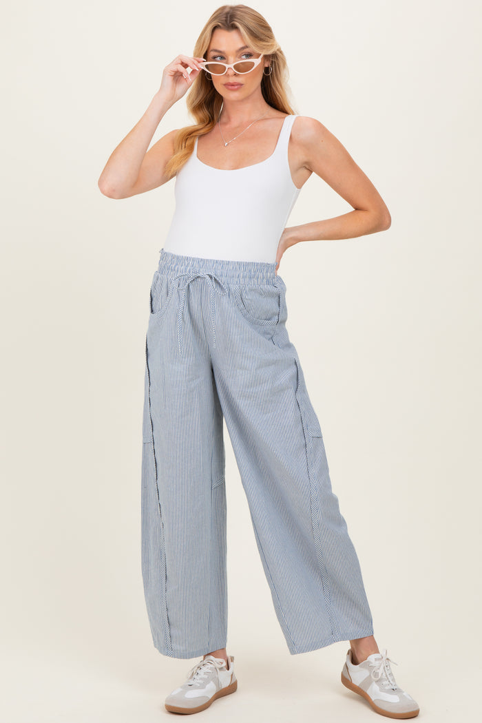 woman wearing a white tank top and light blue striped maternity pants with an elastic waistband and sneakers