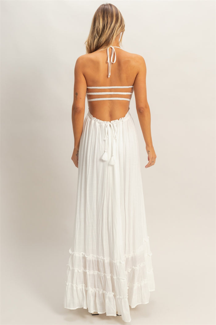 woman wearing a backless white maxi dress with adjustable straps and tiered ruffles at the hem