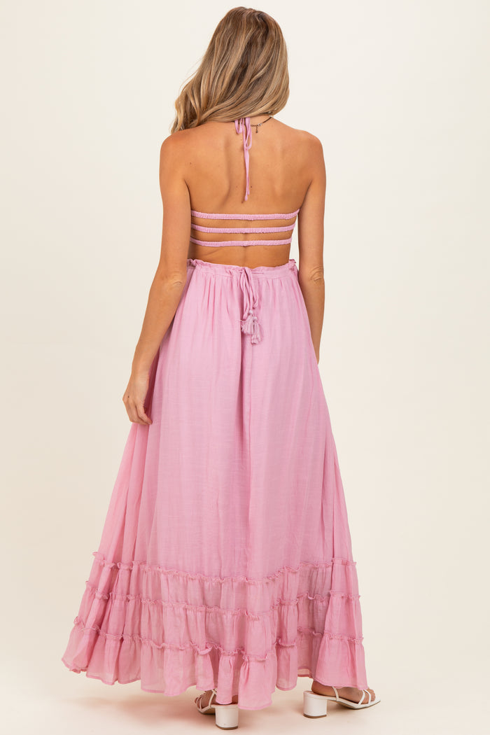 woman wearing a pink maternity maxi dress with a halter neck and tiered ruffle hem, revealed back design