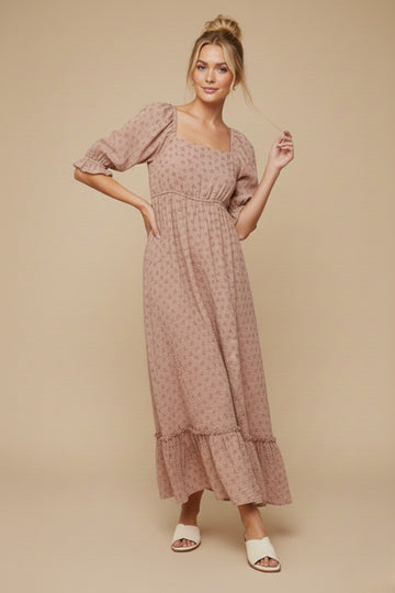 woman wearing a blush pink floral maxi dress with puff sleeves and a tiered hem, standing against a neutral background
