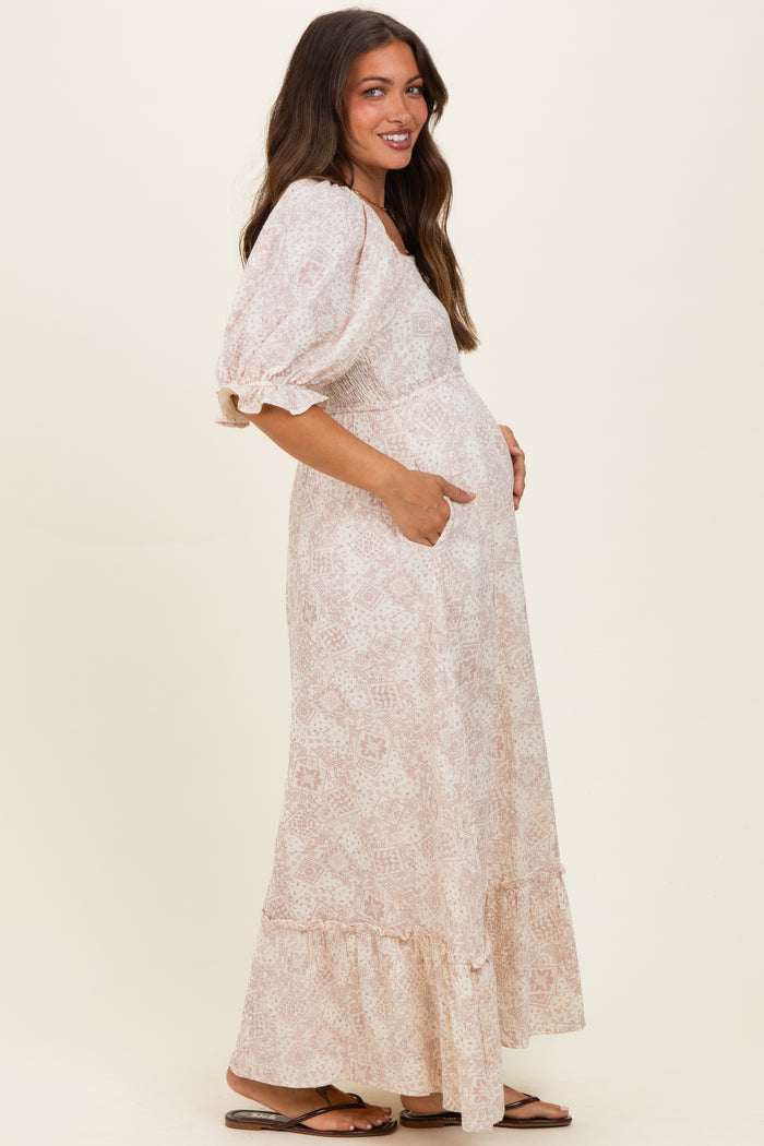 woman wearing a light pink patterned maternity maxi dress with puff sleeves and pockets, showing a baby bump