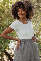 woman wearing a white short sleeve maternity top and a patterned skirt, highlighting her baby bump