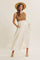woman wearing a brown knit sleeveless dress with a flowy white skirt and a straw hat, posing with hands in pockets