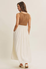 woman wearing a brown knitted tank top with a white flowy maxi skirt, viewed from the back