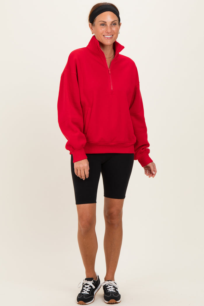 woman wearing a red quarter-zip pullover sweatshirt with black bike shorts and sneakers