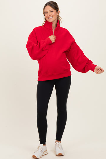 woman wearing a red maternity pullover sweatshirt with a half-zip and balloon sleeves, paired with black leggings and sneakers