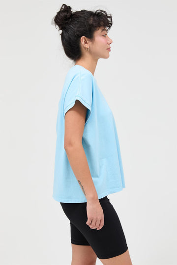 woman wearing a light blue oversized t-shirt and black bike shorts, standing in a side profile view