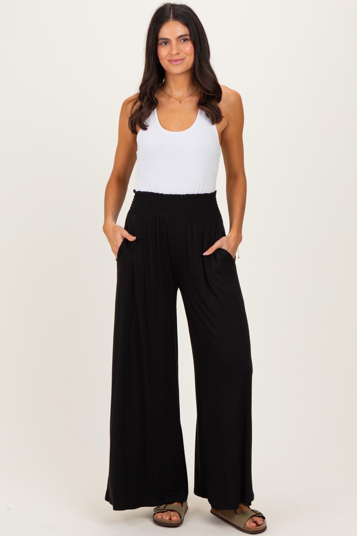 woman wearing a white tank top and black wide-leg pants with a smocked waistband and pockets