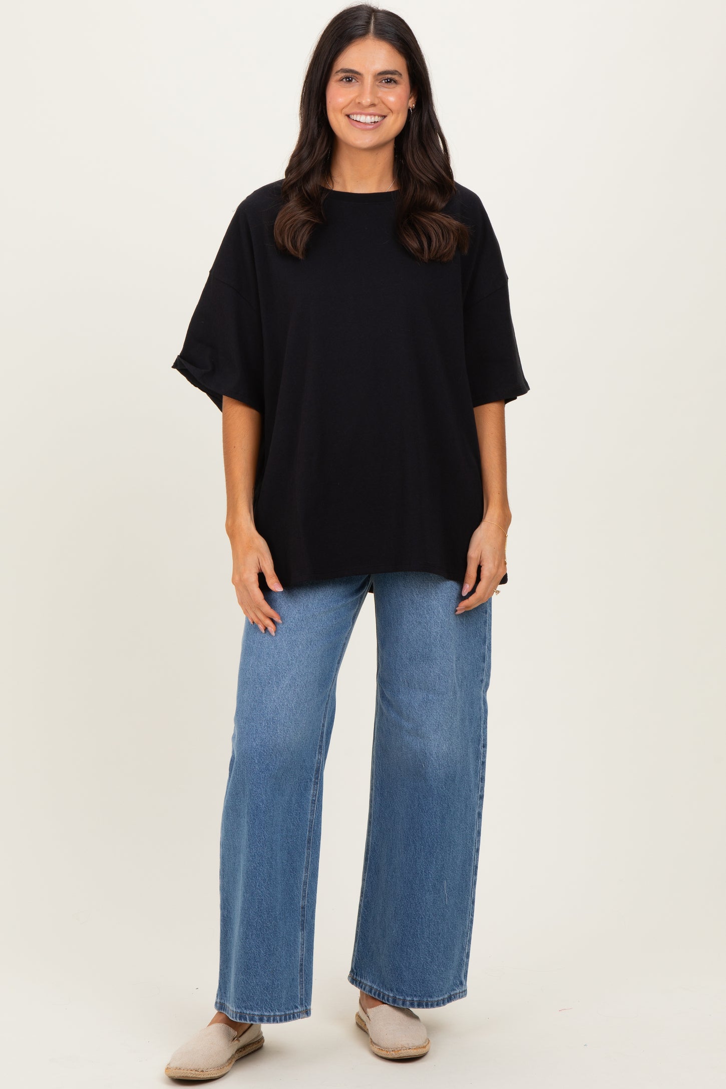 woman wearing a black oversized t-shirt and light blue wide leg jeans with beige slip-on shoes
