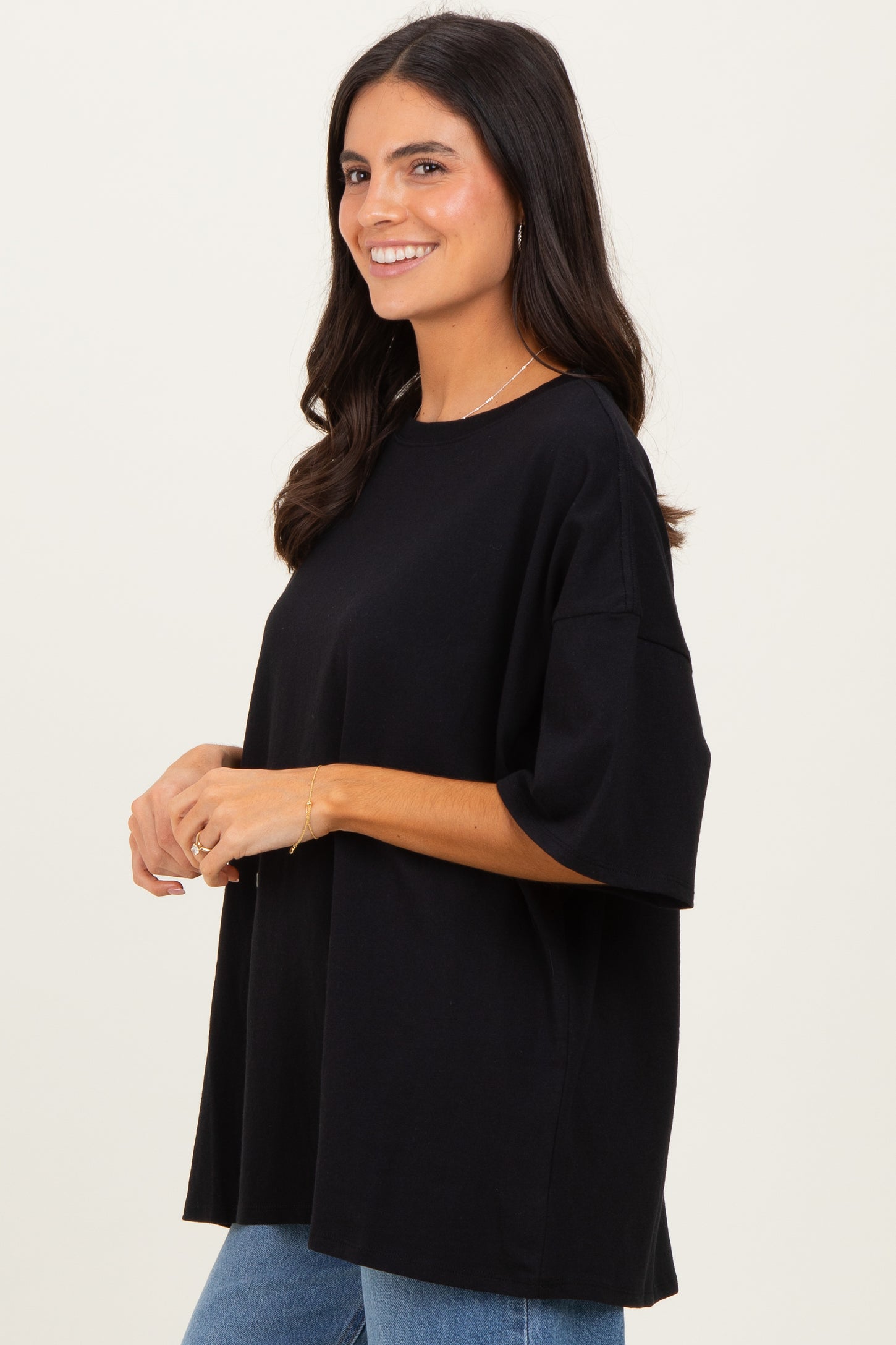 woman wearing a black oversized t-shirt paired with blue jeans, smiling and posing sideways