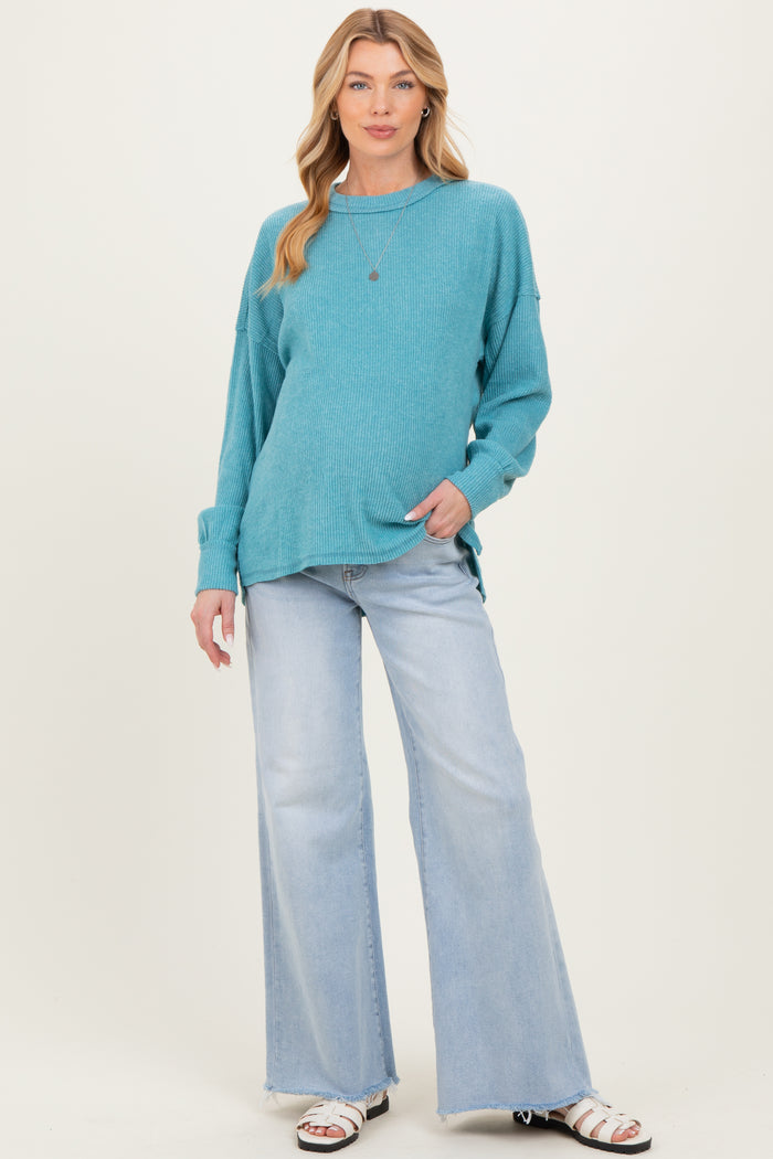 woman wearing a teal maternity sweater with long sleeves and relaxed fit paired with light wash flared jeans