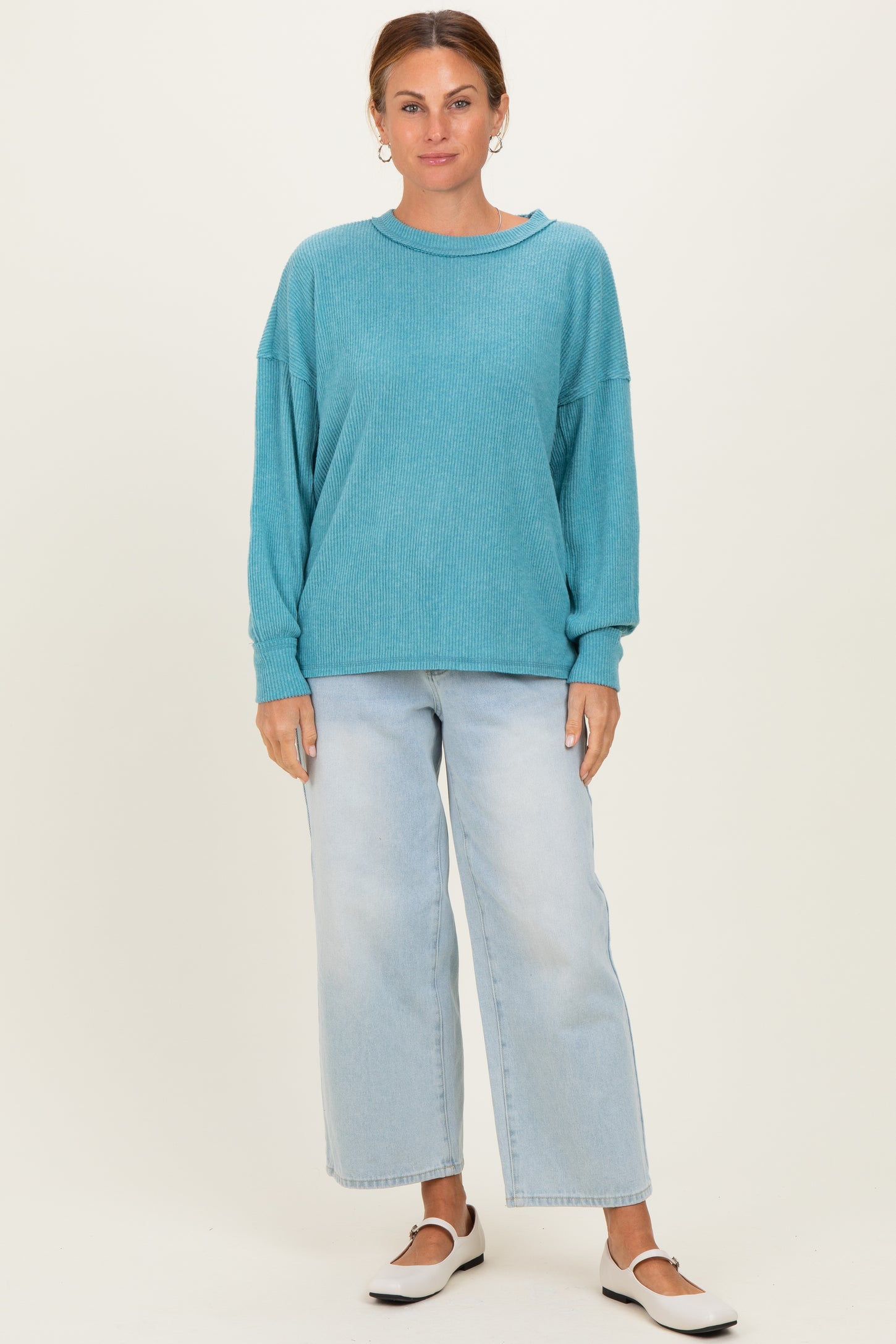 woman wearing a teal oversized ribbed sweater and light wash wide leg jeans with white slip-on shoes
