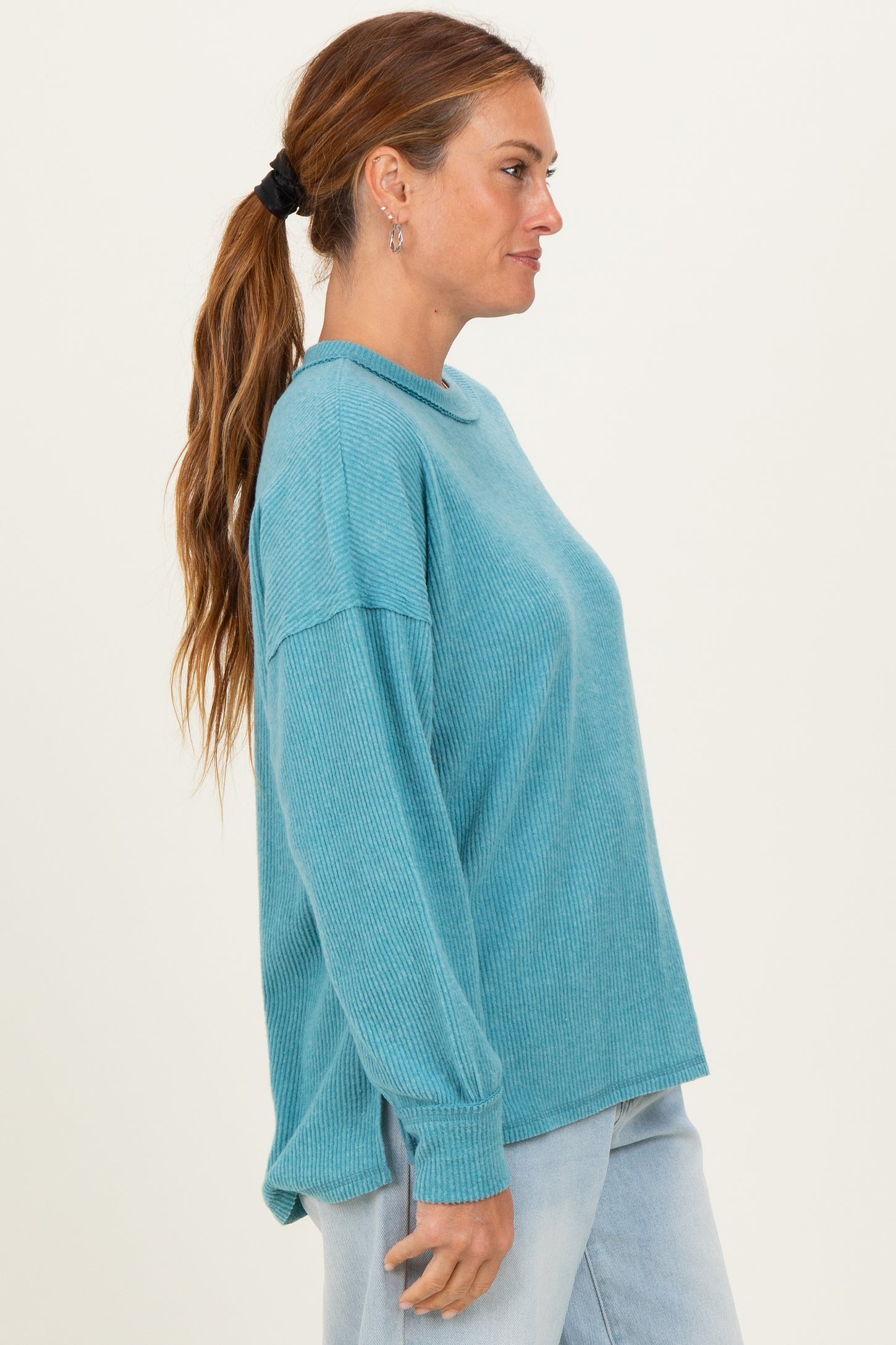 woman wearing a teal ribbed long sleeve top with a relaxed fit and slightly dropped shoulders