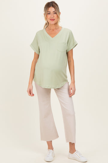 woman wearing a light green v-neck maternity top with a pocket and light beige wide-leg pants, showing her baby bump