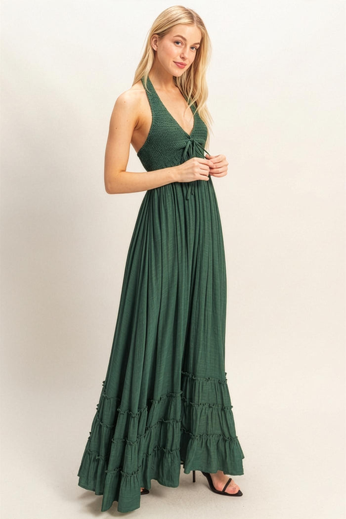 woman wearing a deep green halter neck maxi dress with smocked bodice and tiered ruffles at the hem