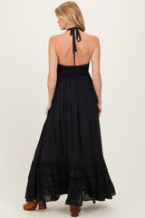 woman wearing a black halter neck maternity maxi dress with a smocked bodice and tiered ruffle hem