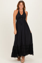 woman wearing a black halter neck maxi dress with a tie front and ruffled hem, standing and smiling